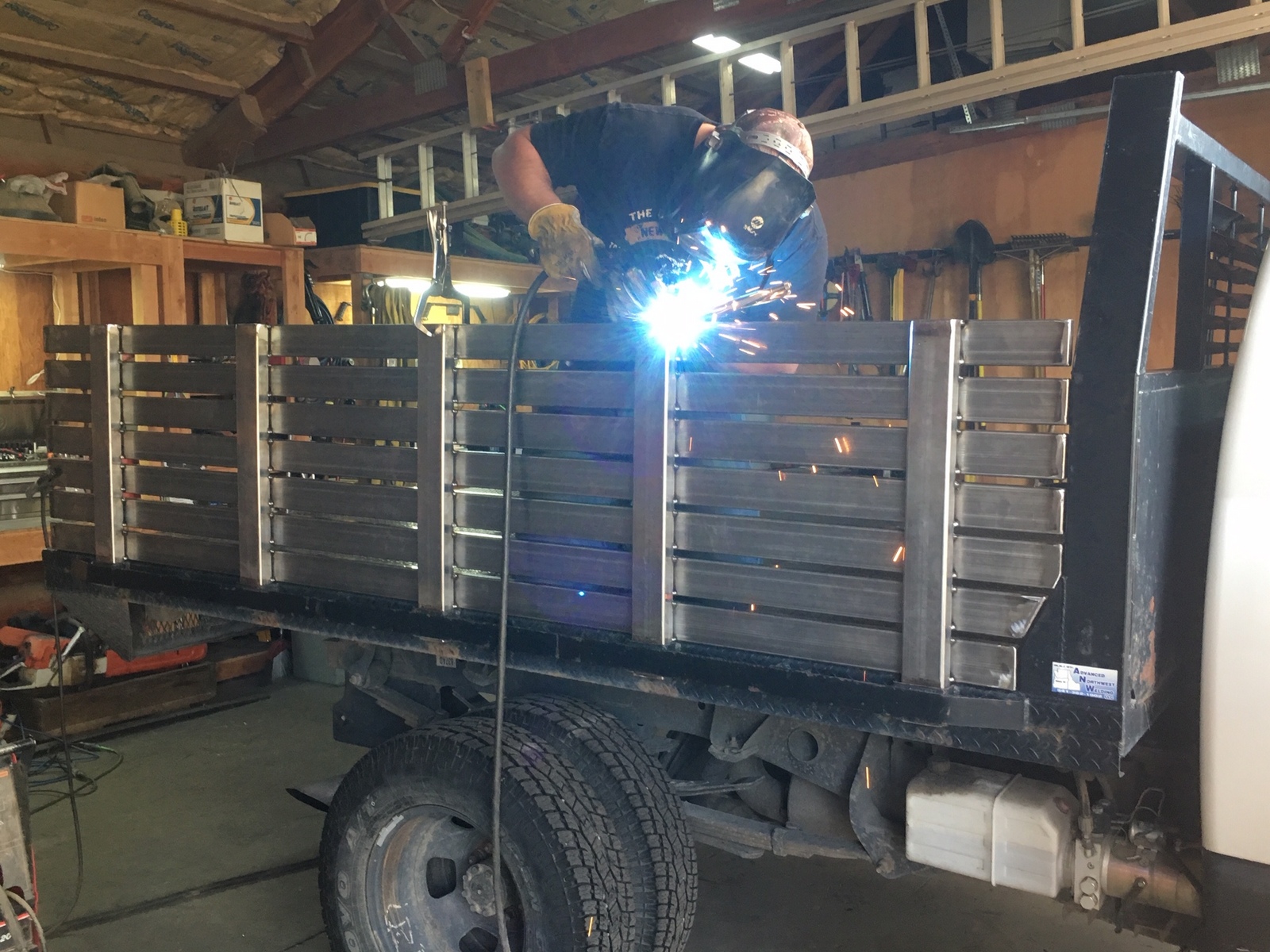 Man in rough building welding steel slats to build truckbed siding